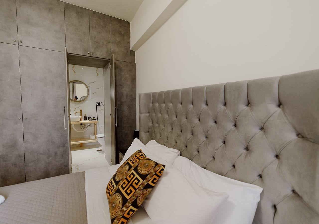 Grey tufted headboard and crisp linen, bathroom beyond